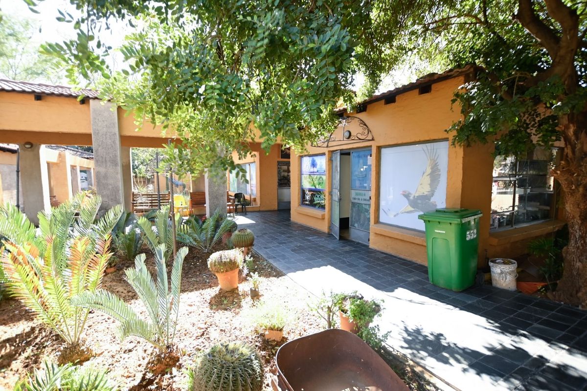 A view of the rear exterior office area featuring a covered walkway, tiled flooring, and established garden landscaping.