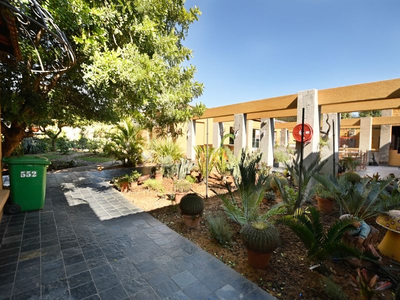 A covered outdoor patio area featuring tiled flooring and a concrete pergola structure, providing a shaded transition space between the building and garden.