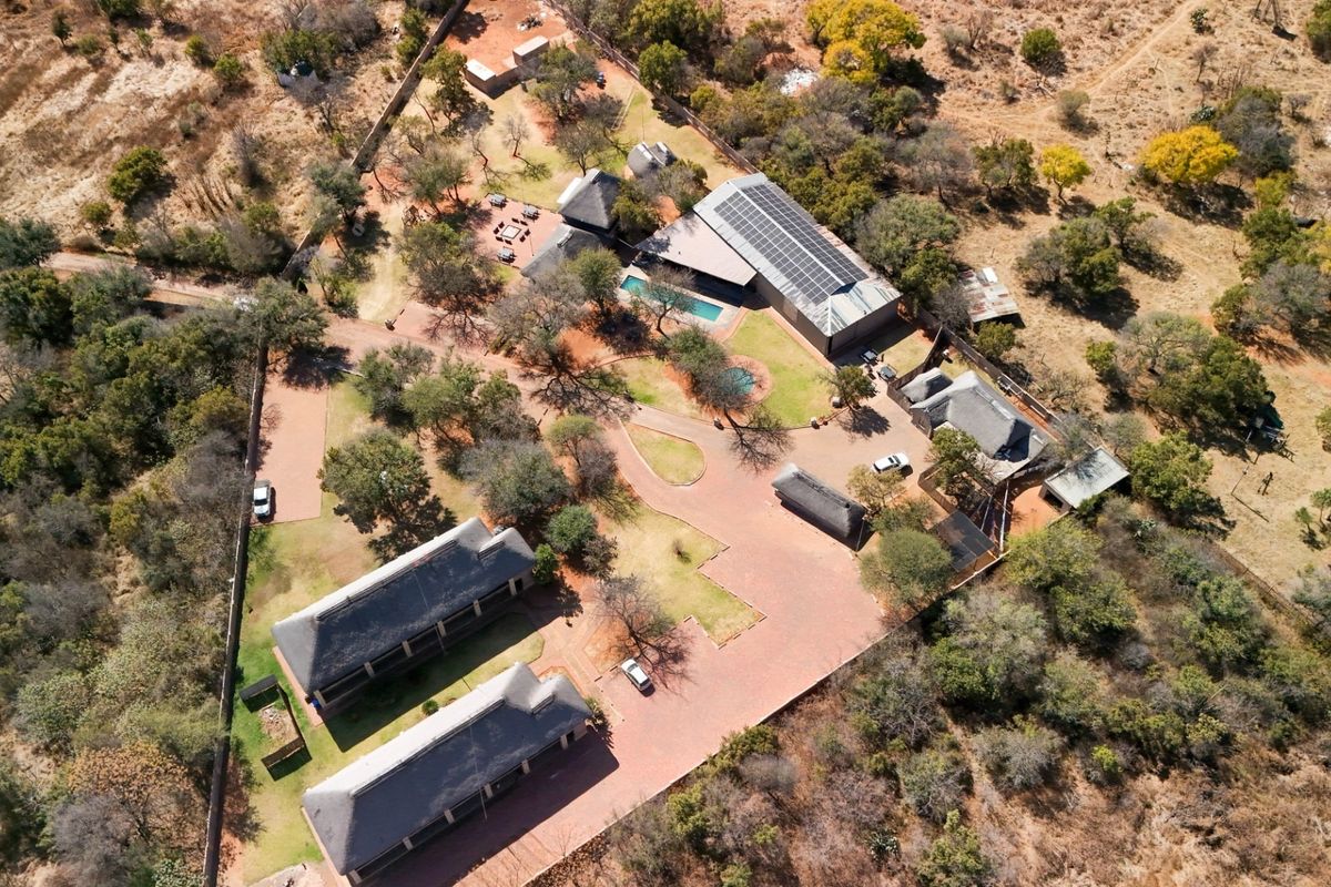 Aerial view of a lodge property featuring multiple thatched-roof buildings, a swimming pool, solar panel installation, and extensive landscaped grounds with paved access.