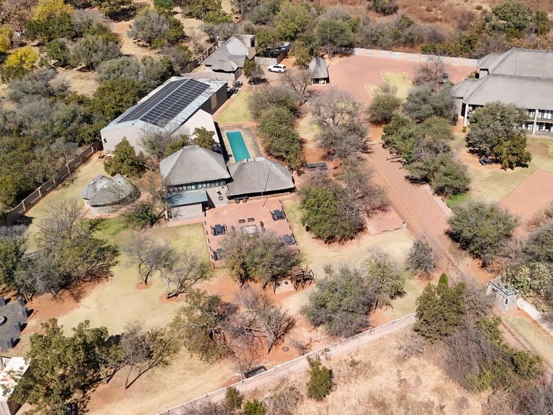 Aerial view of a lodge property featuring multiple buildings with thatched roofs, a swimming pool, solar panels, and extensive landscaped grounds.