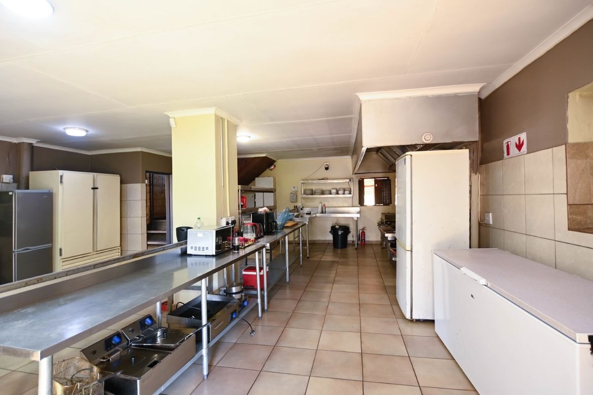 A functional commercial-style kitchen featuring stainless steel prep surfaces, tiled flooring, and an integrated extractor hood, suitable for high-volume food preparation.