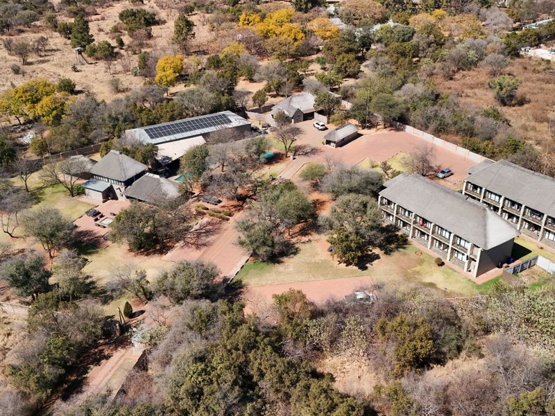 Aerial view of the lodge property featuring multiple buildings with thatched roofs, solar panel installations, paved access paths, and extensive landscaped grounds.