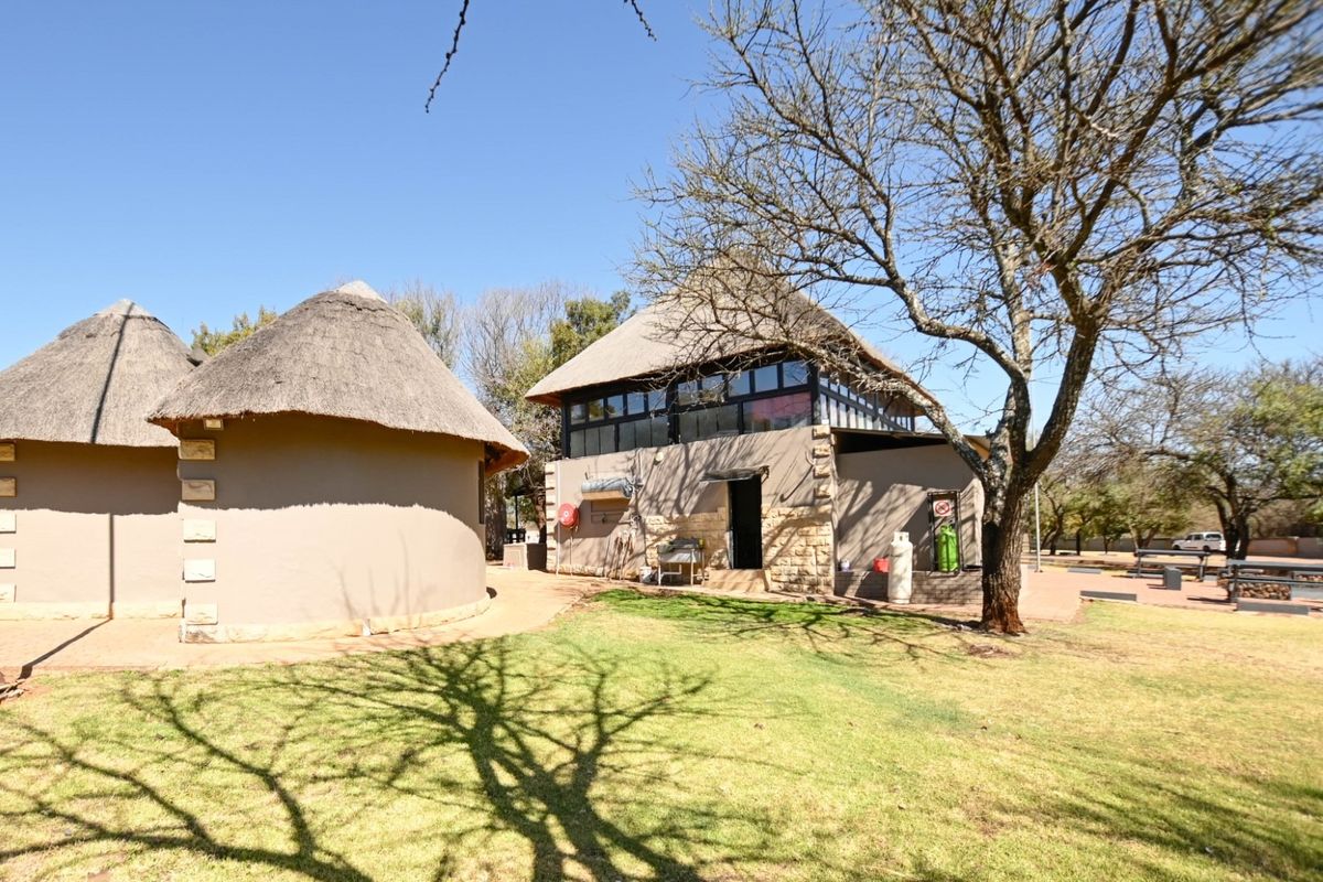 Exterior view of lodge buildings featuring traditional thatch roofing, stone and plaster wall finishes, and surrounding landscaped garden area.