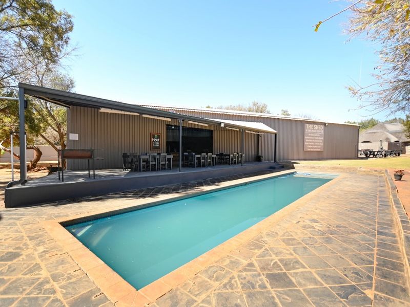 Outdoor pool area featuring a rectangular swimming pool, paved deck, and a covered patio attached to a metal-clad lodge building.