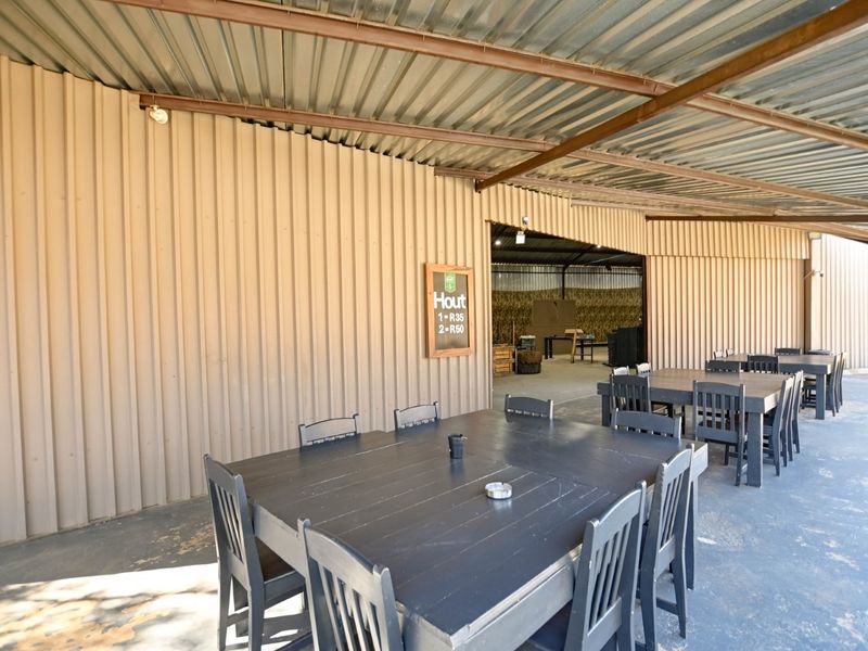A covered outdoor patio area featuring corrugated metal roofing and wall cladding with a concrete floor, suitable for casual dining or social gatherings.