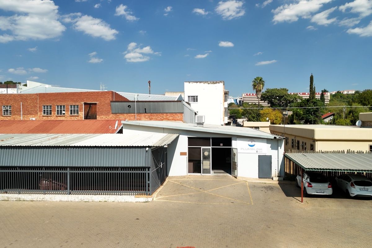 Aerial view of a commercial property featuring a paved driveway, covered carport, and metal security fencing.