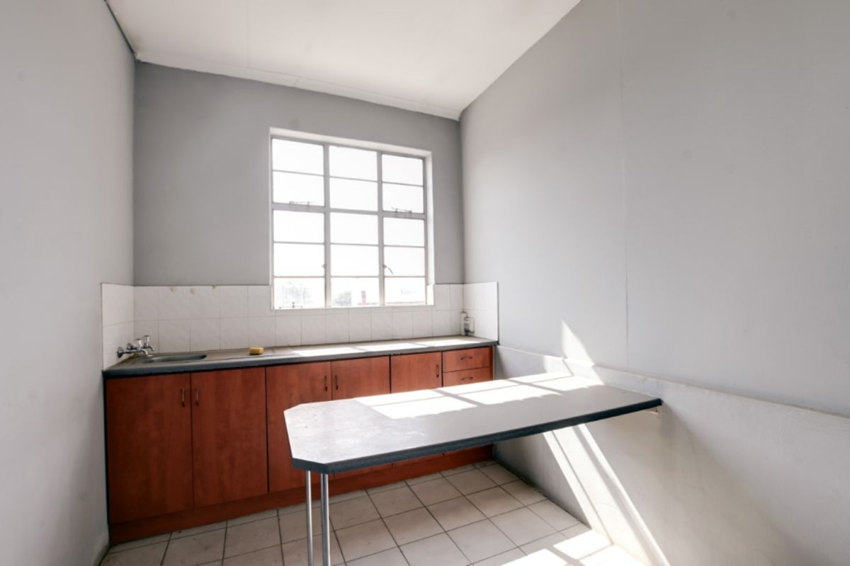 A functional kitchen area featuring built-in wooden cabinetry, a stainless steel sink, tiled backsplash, and a fixed breakfast bar with tiled flooring.