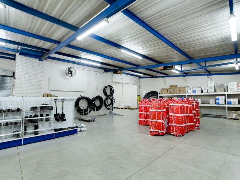 Spacious retail utility or warehouse area featuring exposed steel roof trusses, durable concrete flooring, and integrated shelving units for organized storage.