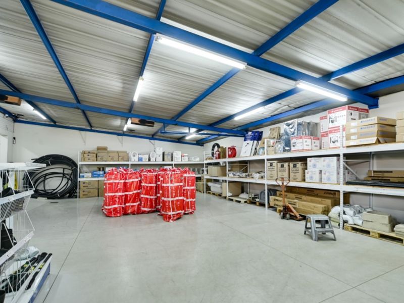 A spacious industrial utility or storage area featuring exposed steel roof trusses, durable concrete flooring, and extensive built-in metal shelving for organized inventory management.