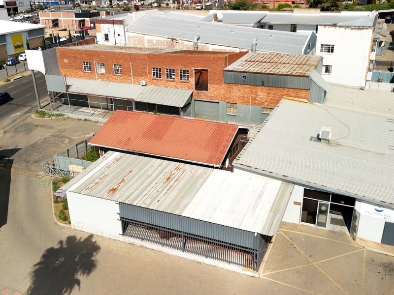 Aerial view of a commercial property complex featuring multiple buildings with corrugated metal roofs, brick facades, and paved access areas.