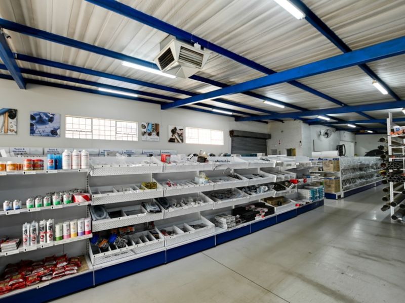 A well-organized retail utility space featuring extensive metal shelving, exposed steel structural beams, and industrial-style lighting, suitable for hardware or commercial inventory storage.