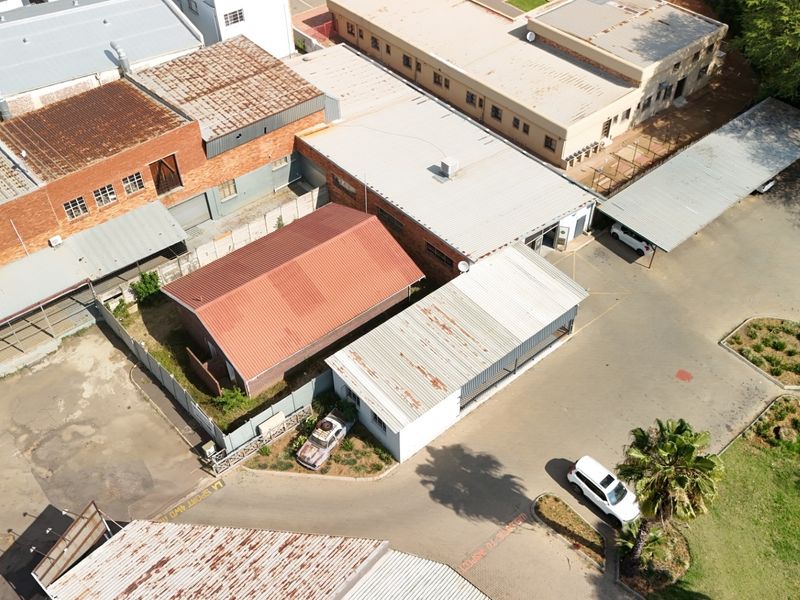 Aerial view of a commercial property complex featuring multiple buildings with corrugated metal roofs, paved parking areas, and perimeter fencing.