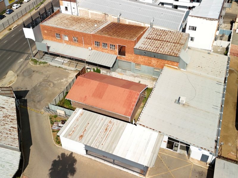 Aerial view of a commercial property complex featuring multiple buildings with corrugated metal roofs, brick facades, and an adjacent asphalt parking area.