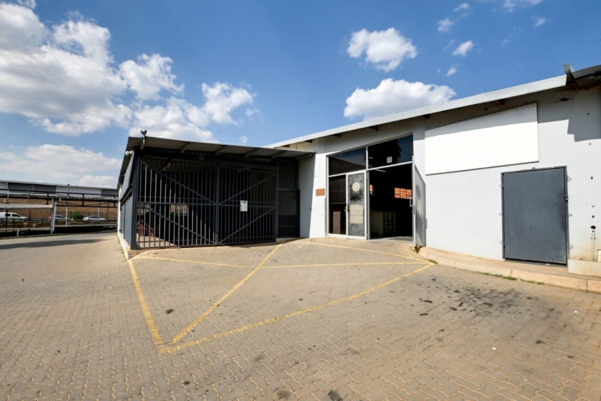 Front exterior view of a commercial retail unit featuring a paved driveway, secure metal gate, and glass entrance door.