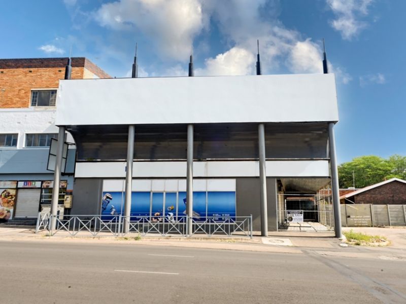 Front elevation of a commercial property featuring a prominent billboard structure, metal support columns, and a glass storefront at street level.