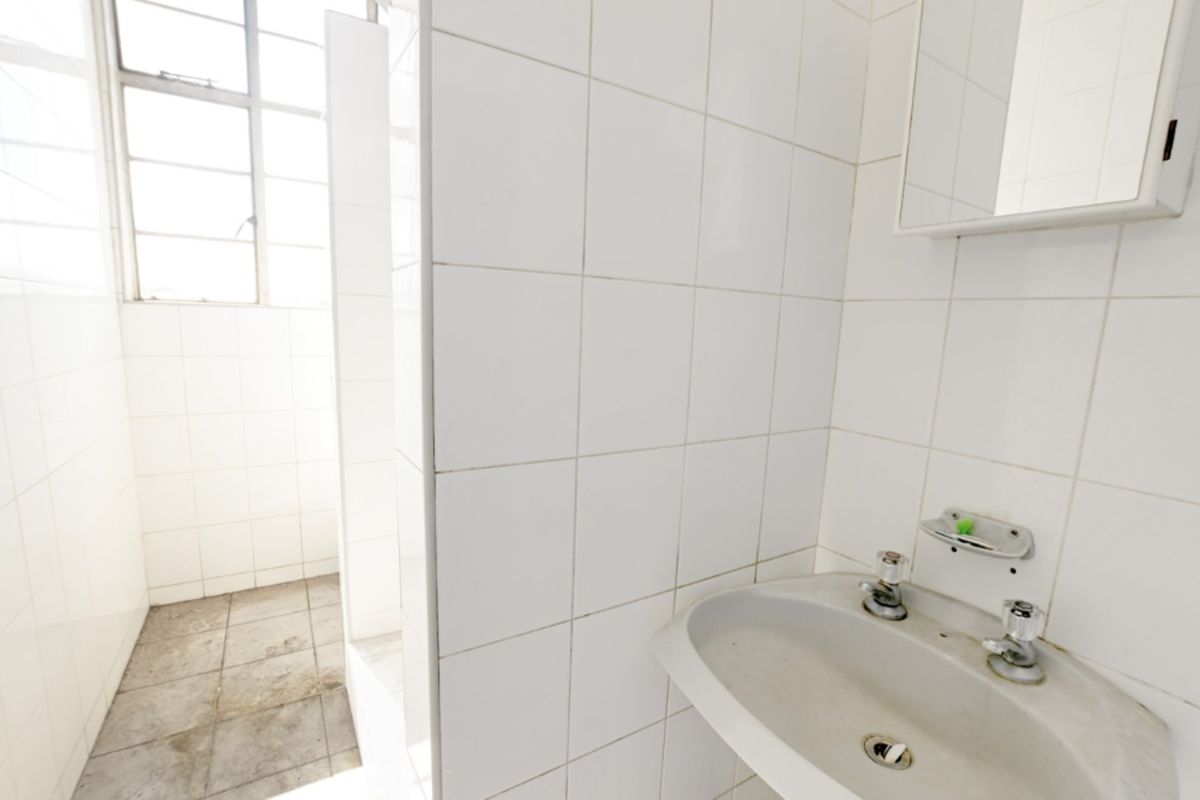 A functional bathroom featuring white wall tiles, a wall-mounted basin, and a metal-framed window, requiring cosmetic updates to improve its overall condition.