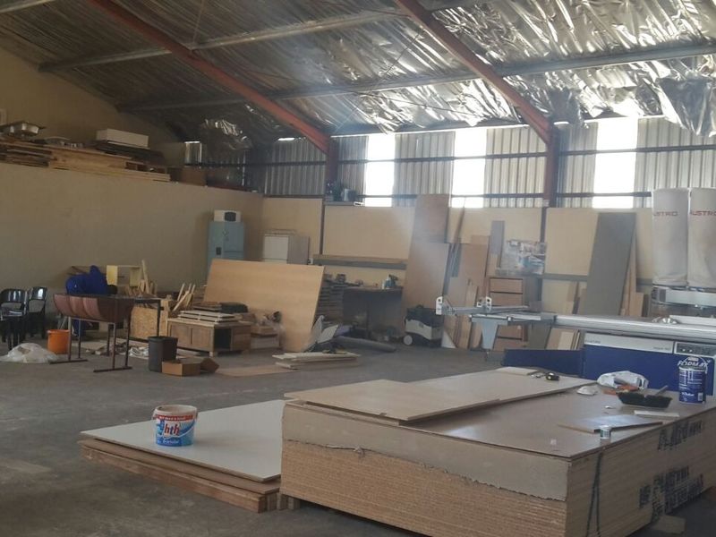 Spacious industrial utility area featuring exposed steel roof trusses, concrete flooring, and high-level windows, suitable for workshop or storage operations.
