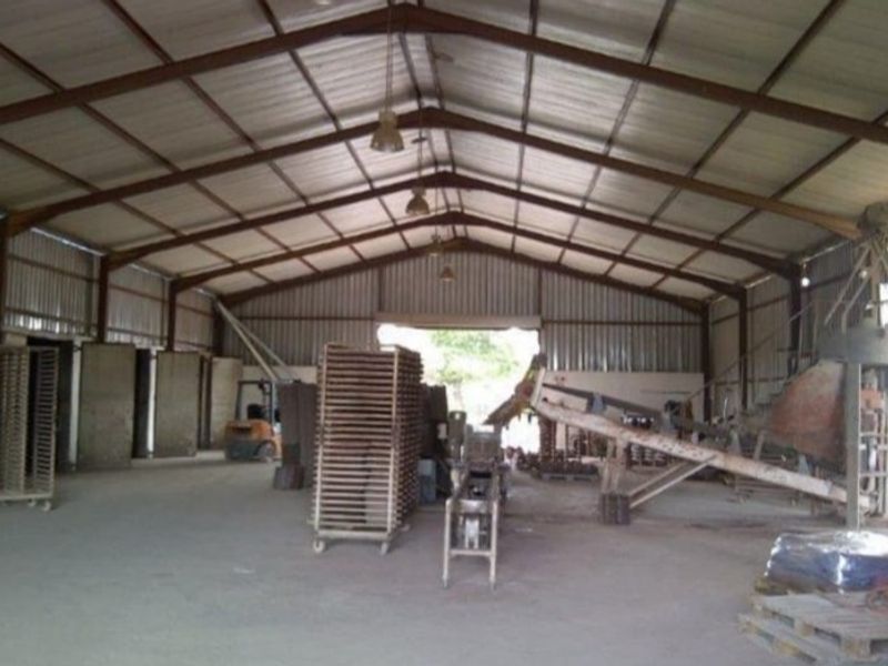 Spacious industrial warehouse featuring a steel portal frame, corrugated metal walls, concrete flooring, and high-clearance gabled roof structure suitable for manufacturing or storage operations.