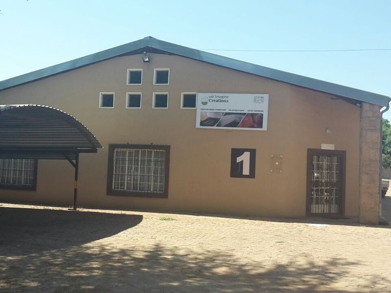 Front elevation of an industrial building featuring a covered carport, security bars on windows, and prominent signage on the facade.