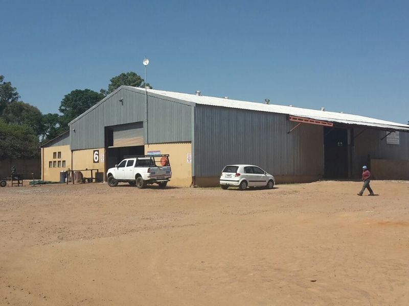 Industrial warehouse facility featuring corrugated metal cladding, large roller shutter access doors, and a spacious unpaved yard area.