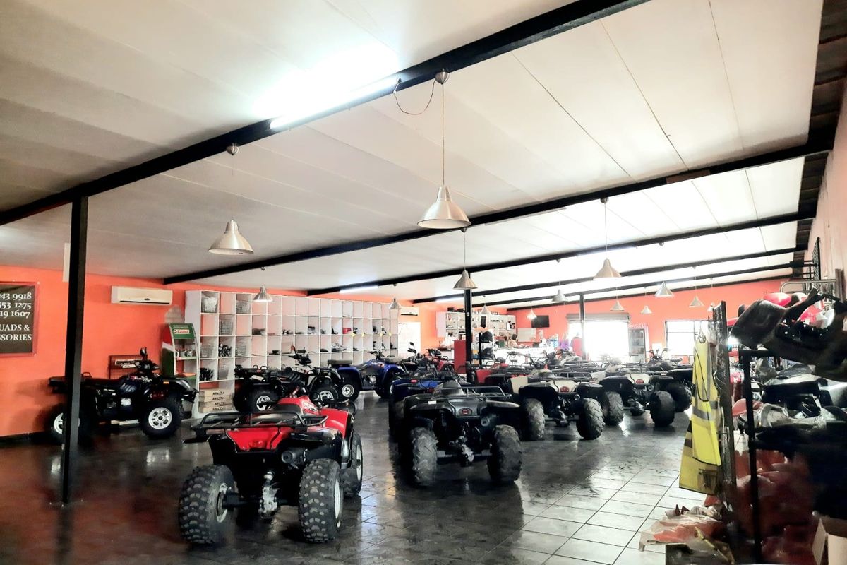 Spacious open-plan retail showroom featuring tiled flooring, exposed steel structural beams, built-in shelving, and industrial pendant lighting.