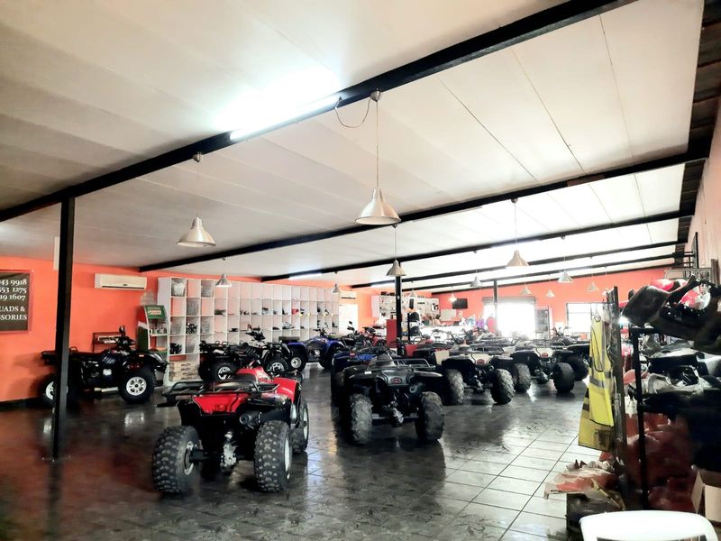 Spacious open-plan retail showroom featuring tiled flooring, exposed steel structural beams, built-in shelving, and industrial pendant lighting.