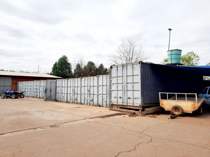Exterior view of a commercial yard featuring multiple shipping containers used for storage, a water tank, and a paved concrete surface.
