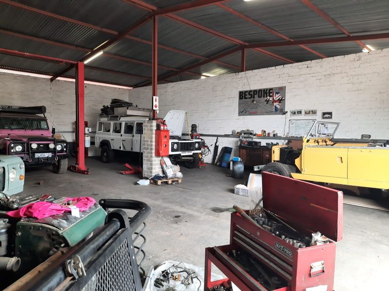 Spacious industrial-style workshop or garage featuring exposed steel roof trusses, corrugated metal roofing, and durable concrete flooring, suitable for automotive or utility use.