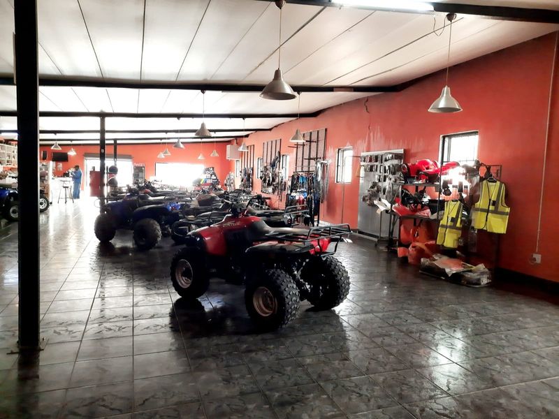 Spacious retail utility area featuring tiled flooring, exposed structural beams, and wall-mounted display systems, currently utilized for vehicle storage and display.