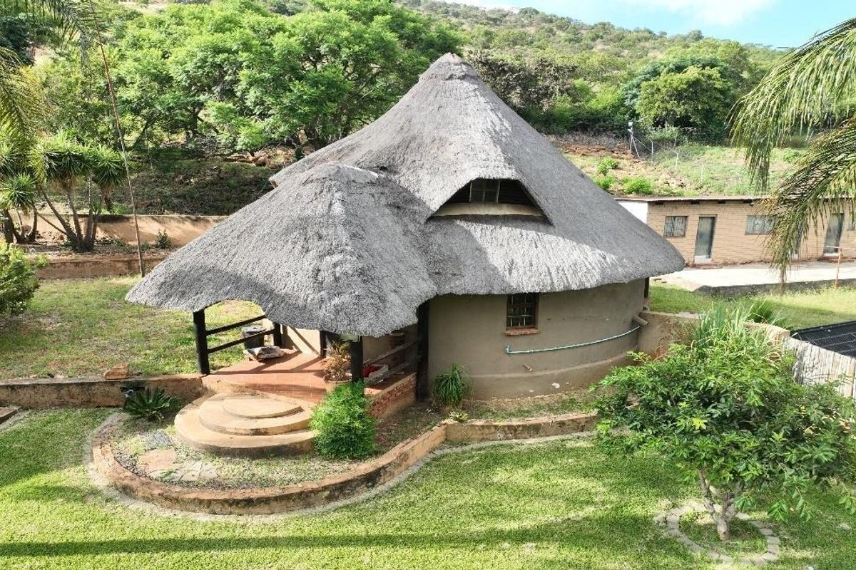 A rear view of a rustic farmhouse featuring a traditional thatched roof, a covered patio area, and landscaped garden surroundings.
