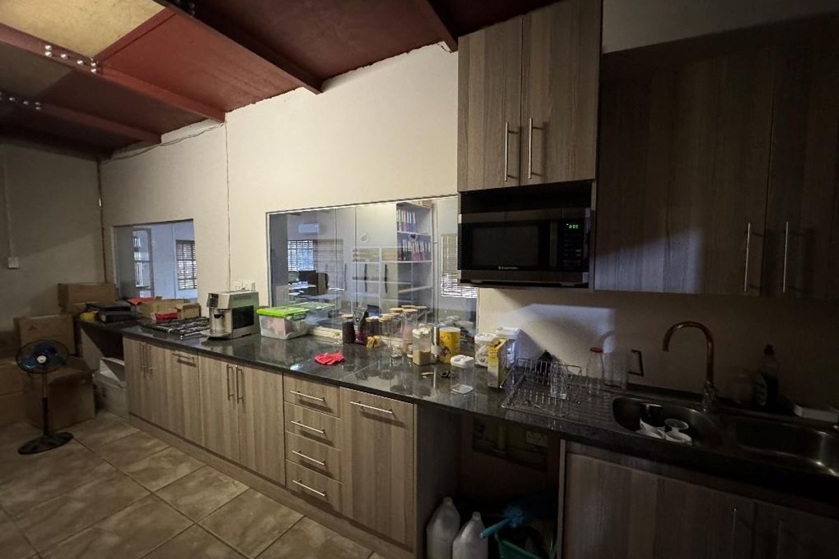A functional kitchen area featuring wood-look cabinetry, granite-style countertops, a built-in microwave, and exposed industrial-style steel roof beams.