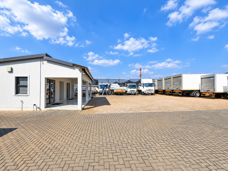 Exterior view of an office building featuring a paved driveway, covered patio area, and ample space for vehicle parking.