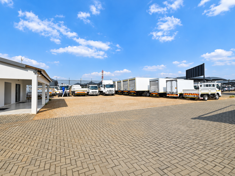 Spacious exterior yard area featuring paved and gravel surfaces, a covered patio section, and ample space for commercial vehicle parking.