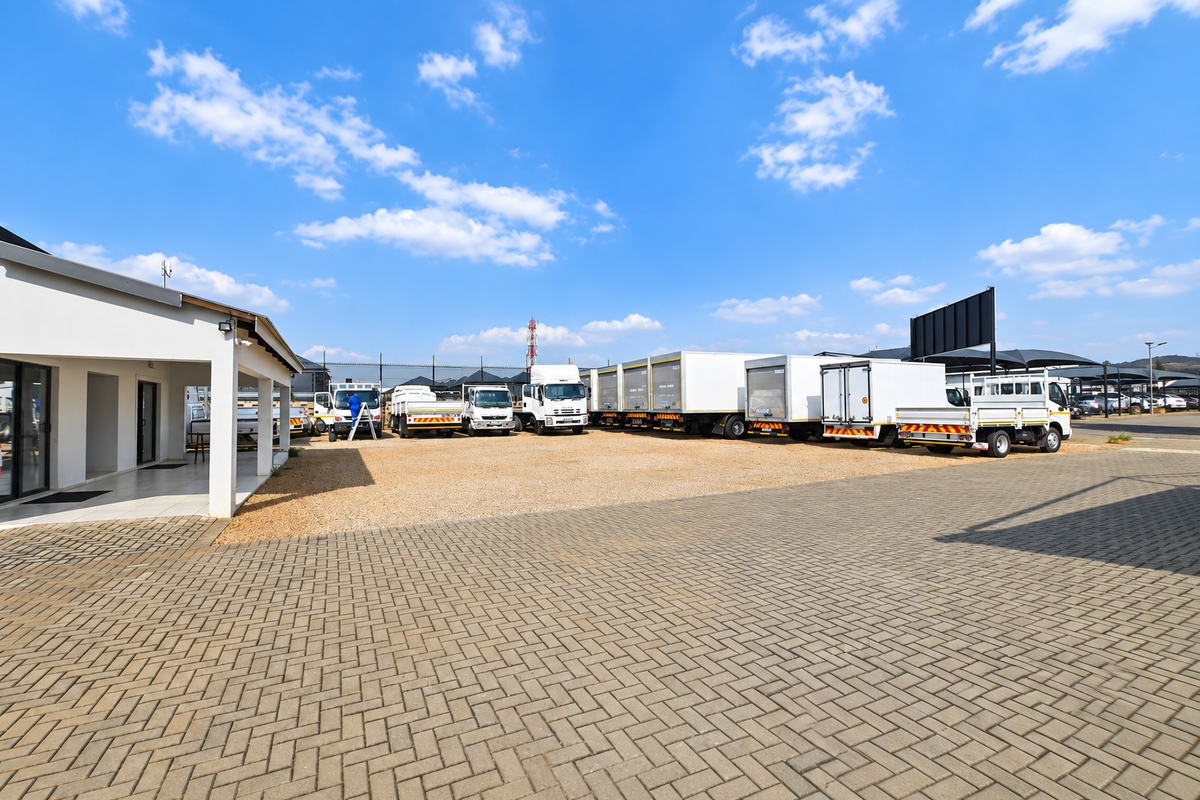 Spacious exterior yard area featuring paved and gravel surfaces, a covered patio section, and ample space for commercial vehicle parking.