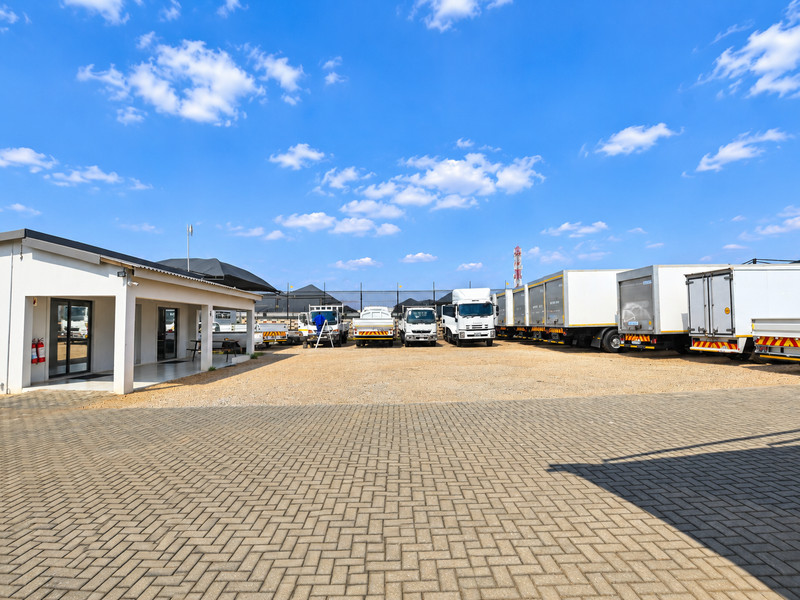 Exterior view of an office building featuring a paved driveway, gravel yard, and covered entrance, with ample space for commercial vehicle parking.