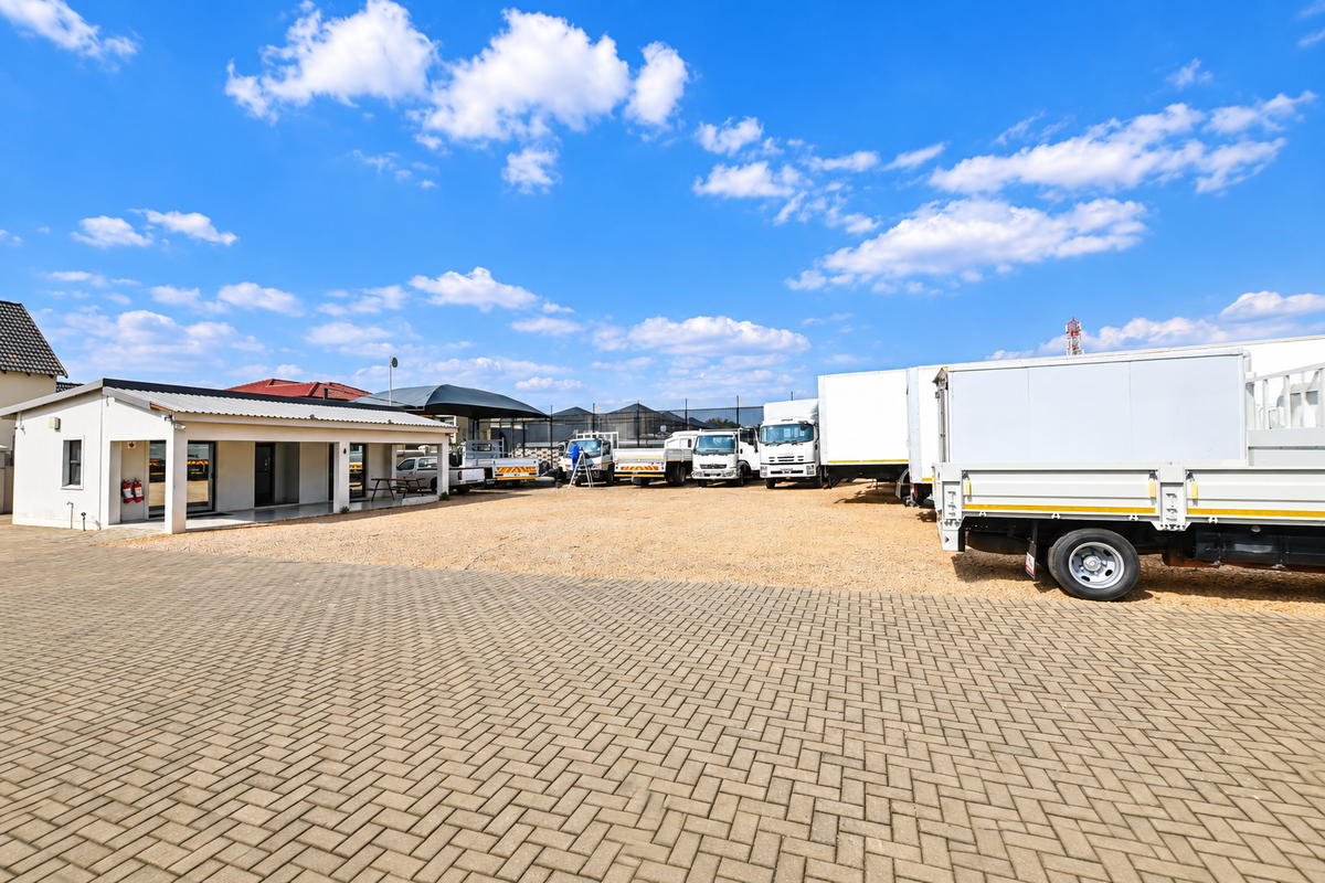 Spacious commercial property exterior featuring a paved driveway, gravel yard area, and a covered patio entrance.