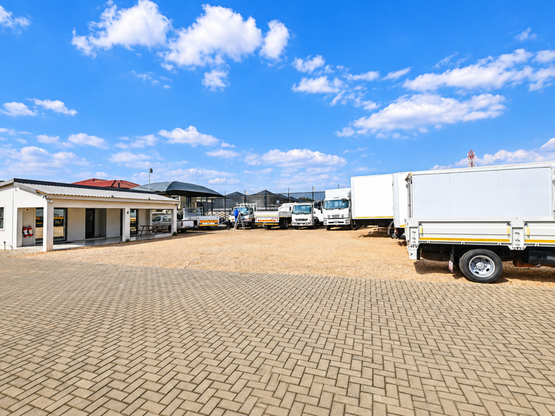 Spacious commercial property exterior featuring a paved driveway, gravel yard area, and a covered patio entrance.