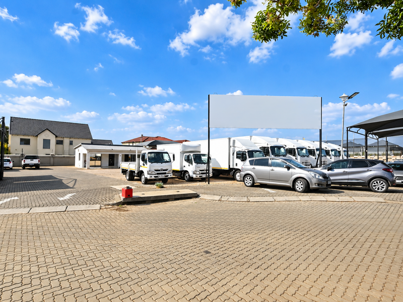 A spacious paved commercial parking area featuring multiple shade cloth carports, perimeter fencing, and a prominent billboard for signage.