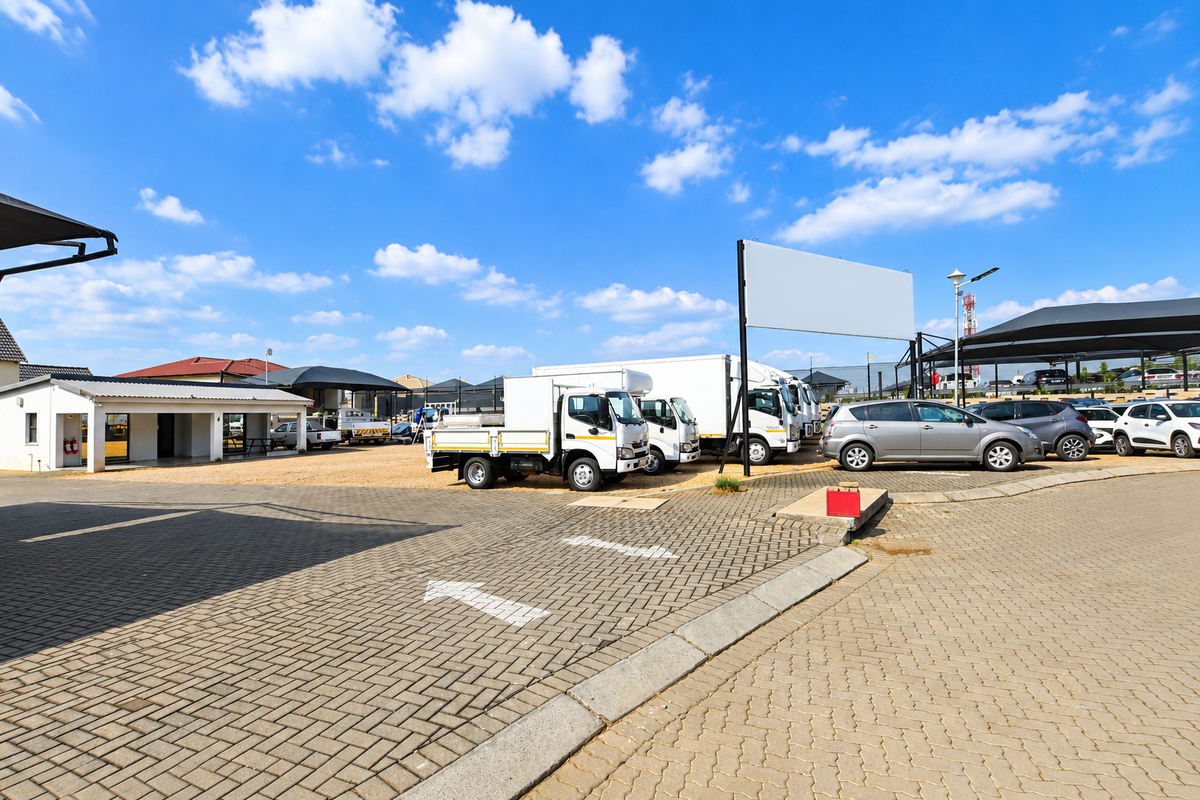 A commercial office property exterior featuring a paved parking area, covered parking bays, and a prominent billboard structure.