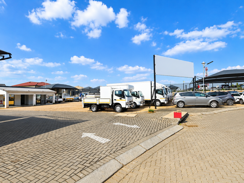 A commercial office property exterior featuring a paved parking area, covered parking bays, and a prominent billboard structure.