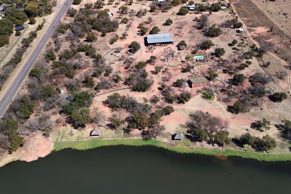 Aerial view of a large commercial vacant land property featuring waterfront access, multiple structures, a swimming pool, and established trees along the shoreline.