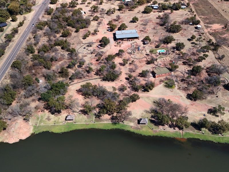 Aerial view of a large commercial vacant land property featuring waterfront access, multiple structures, a swimming pool, and established trees along the shoreline.