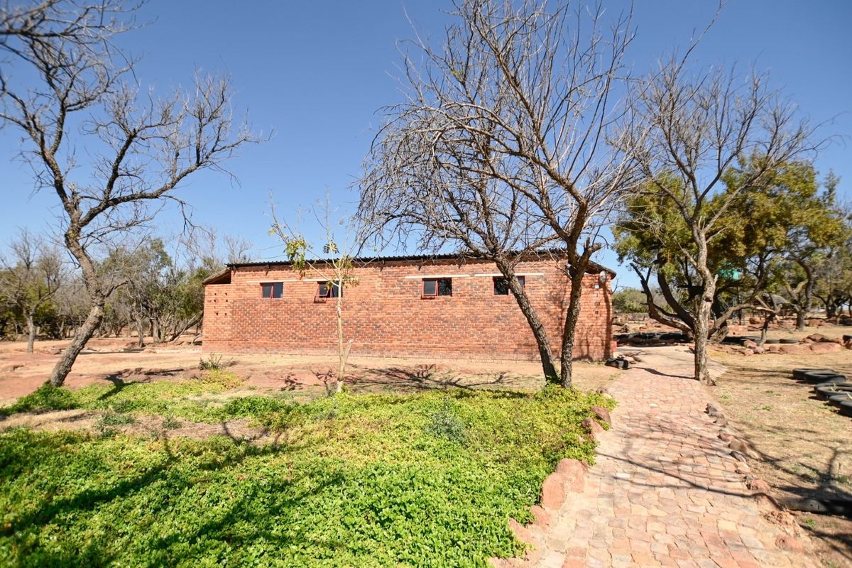 A view of the rear brick structure on the commercial land, featuring a paved walkway and surrounding natural landscape.