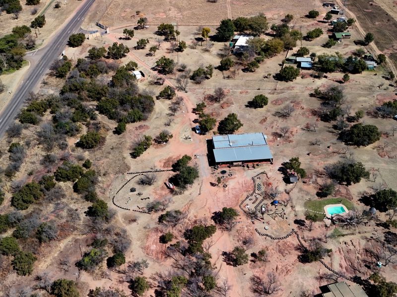 Aerial view of a large commercial vacant land plot featuring a central structure, swimming pool, and extensive natural landscape with road access.