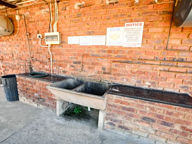 Outdoor utility area featuring a double concrete wash trough, exposed brick walls, and external plumbing and electrical infrastructure.