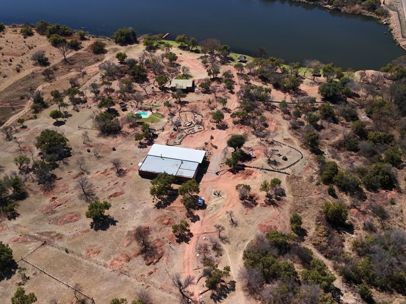 Aerial view of a large vacant commercial land plot featuring a main structure, swimming pool, and direct access to a nearby river and road.