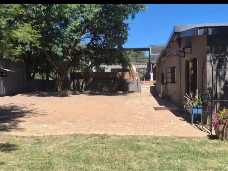 A spacious paved rear courtyard area featuring a shipping container structure, mature trees, and a brick retaining wall on a farm property.