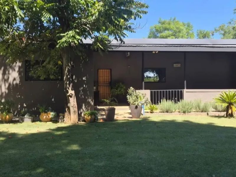 A view of the rear exterior of the farm property, featuring a covered patio area, metal roofing, and a well-maintained garden.