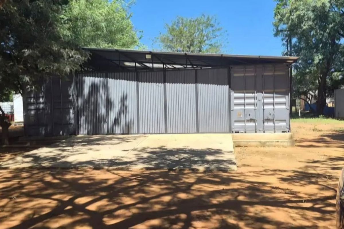A functional garage structure constructed from shipping containers with corrugated metal cladding and a concrete apron, situated on a farm property.