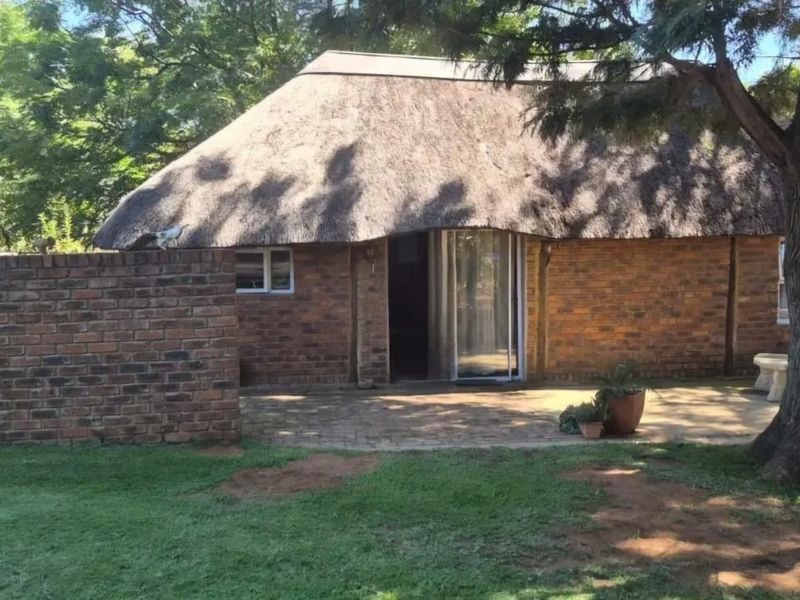 A rear view of a farm-style dwelling featuring a traditional thatched roof, face brick facade, and a paved patio area set within a garden.